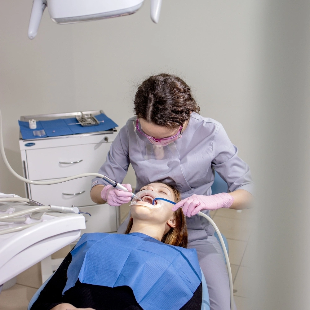 A dentist at Dental Art Clinic in Cambridge performing a professional dental cleaning on a patient using specialized tools while the patient lies comfortably in the dental chair.