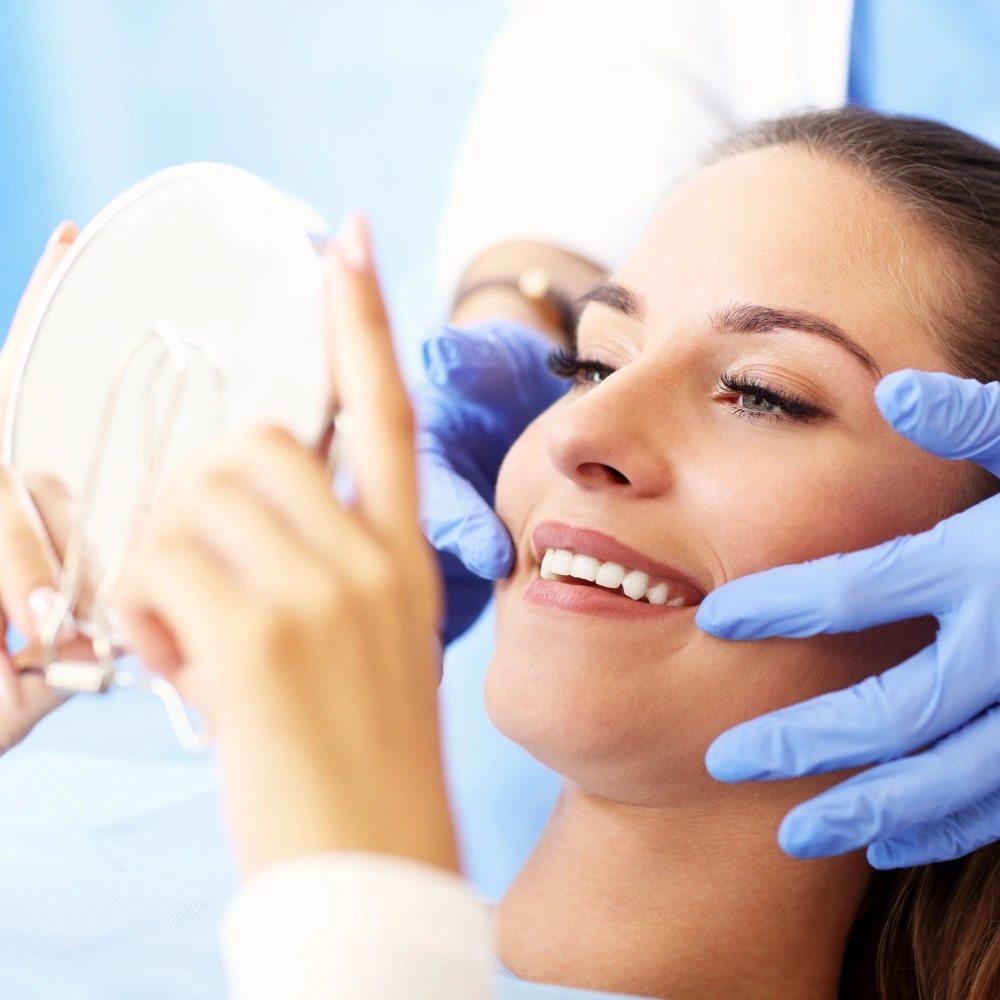 Woman checking her smile in a mirror after a successful root canal treatment at Dental Art Clinic in Cambridge.