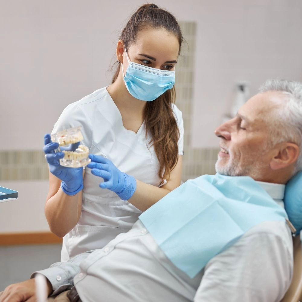 Dentist showing a dental implant model to a senior patient during consultation at Dental Art Clinic in Cambridge.