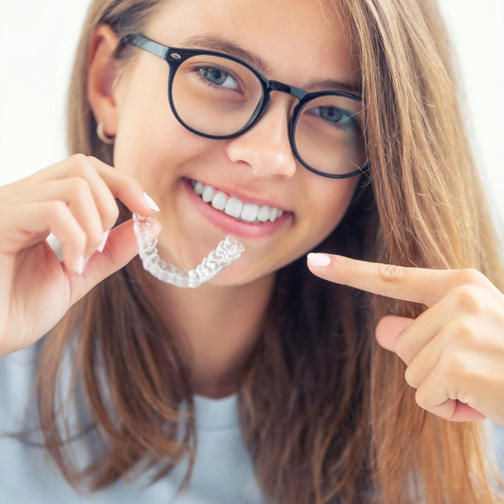 Teen patient smiling while holding a clear aligner at Dental Art Clinic in Cambridge