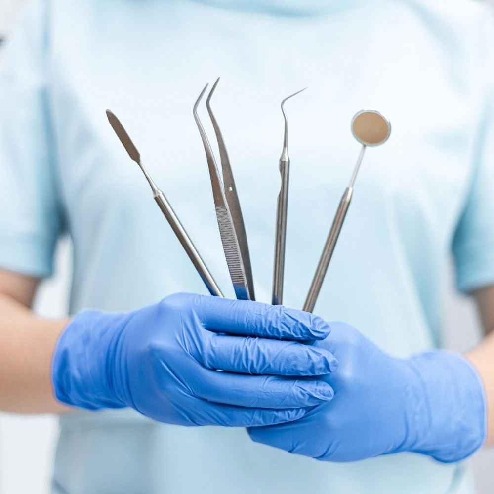 A dental professional holding essential dental examination tools while wearing blue gloves at Dental Art Clinic in Cambridge.