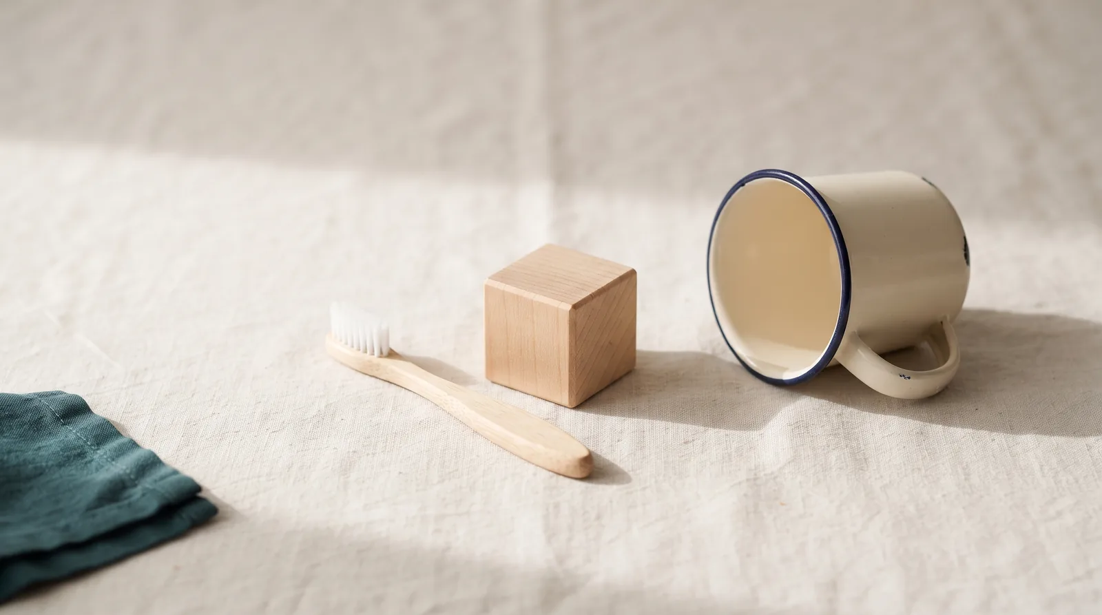 A child-sized toothbrush, a wooden toy block and a small rinse cup on linen