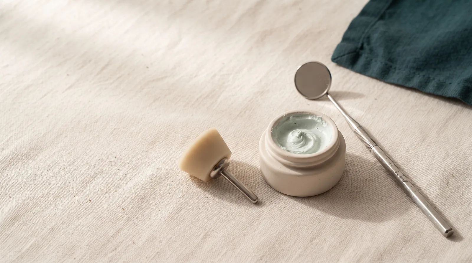 A polishing cup, a small pot of prophy paste and a mirror handle on linen
