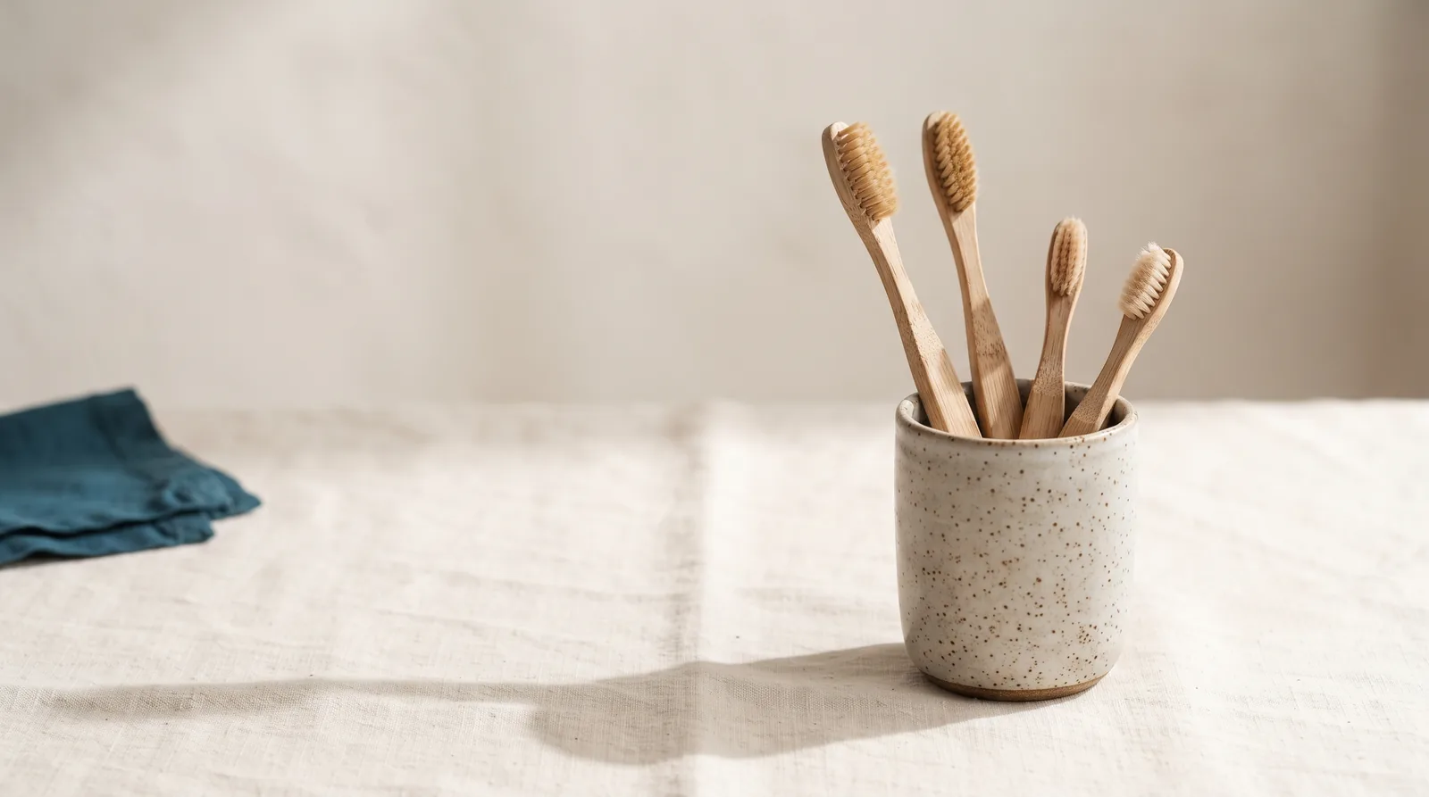 Four toothbrushes of descending size standing together in a ceramic cup on linen