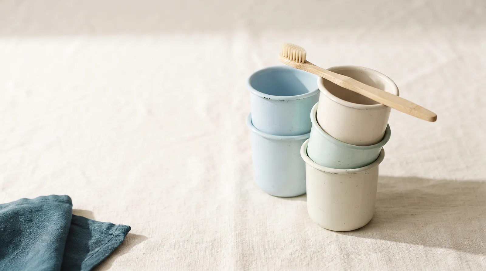 A stack of small enamel rinse cups and a child's toothbrush on linen