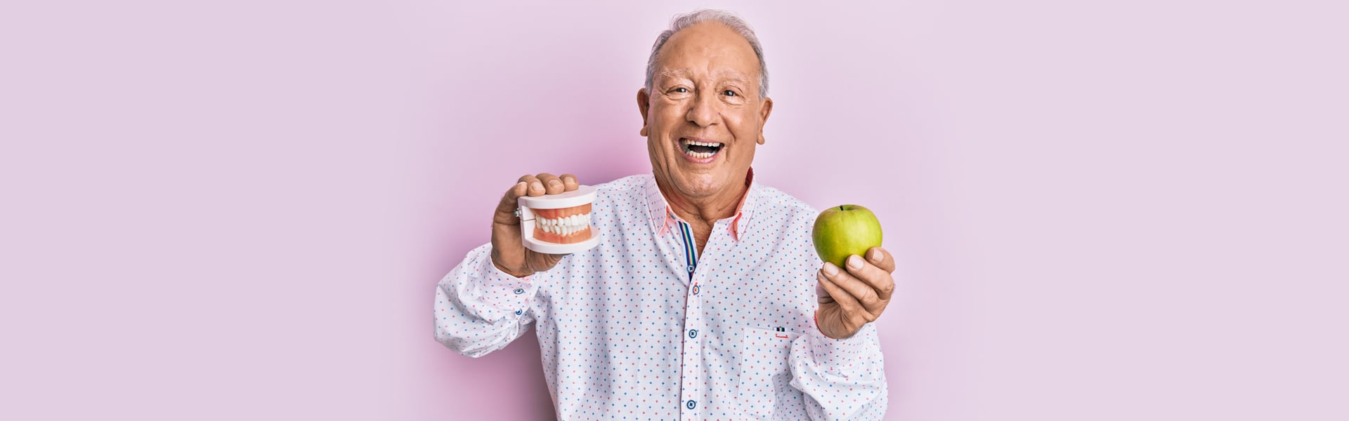 Senior man holding dentures and apple after dental care in Cambridge