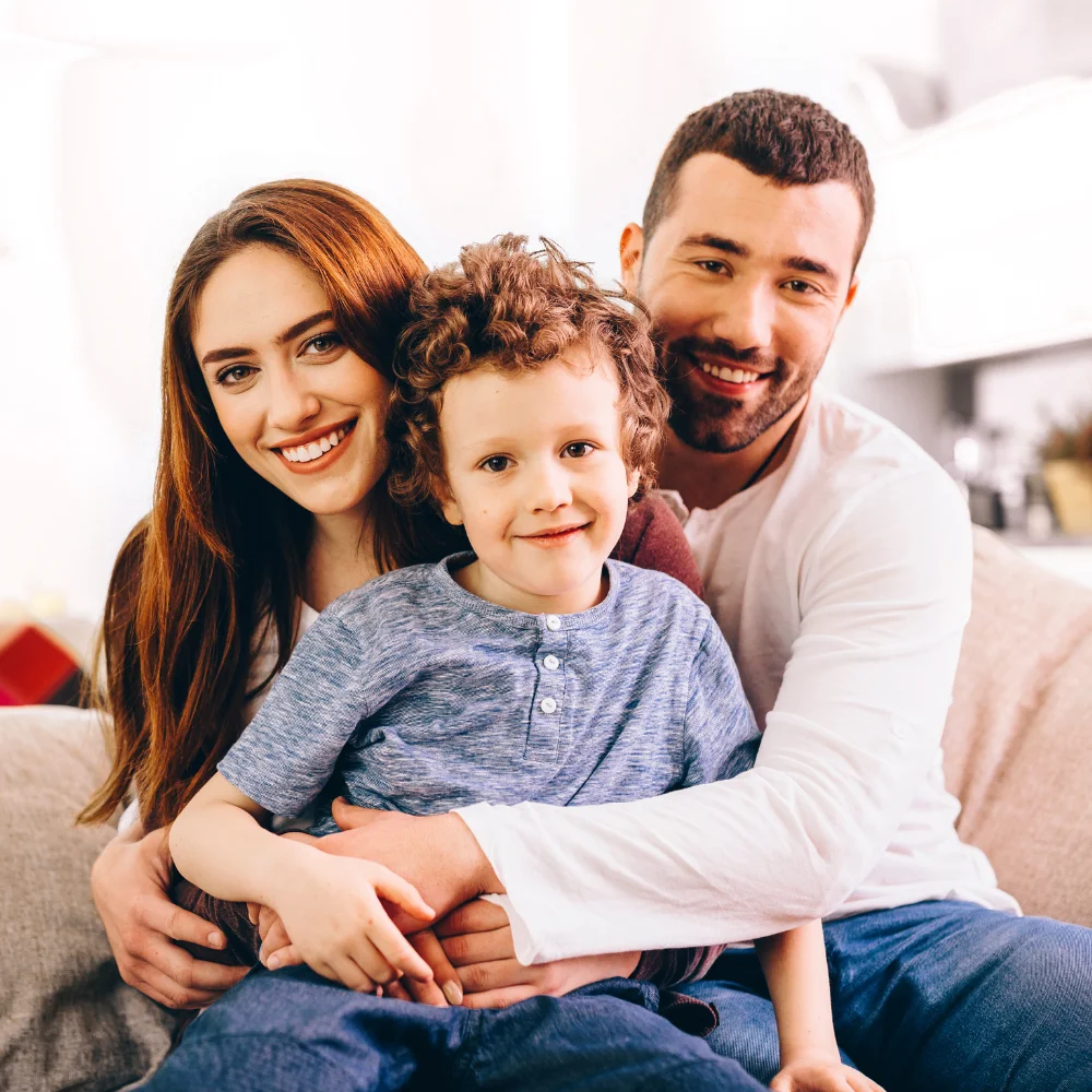 Parents and their young son sitting together on a sofa, all smiling