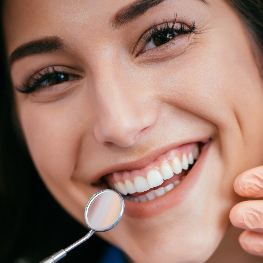 Close-up of a woman smiling during a dental exam with a dentist using a mirror at Dental Art Clinic in Cambridge.