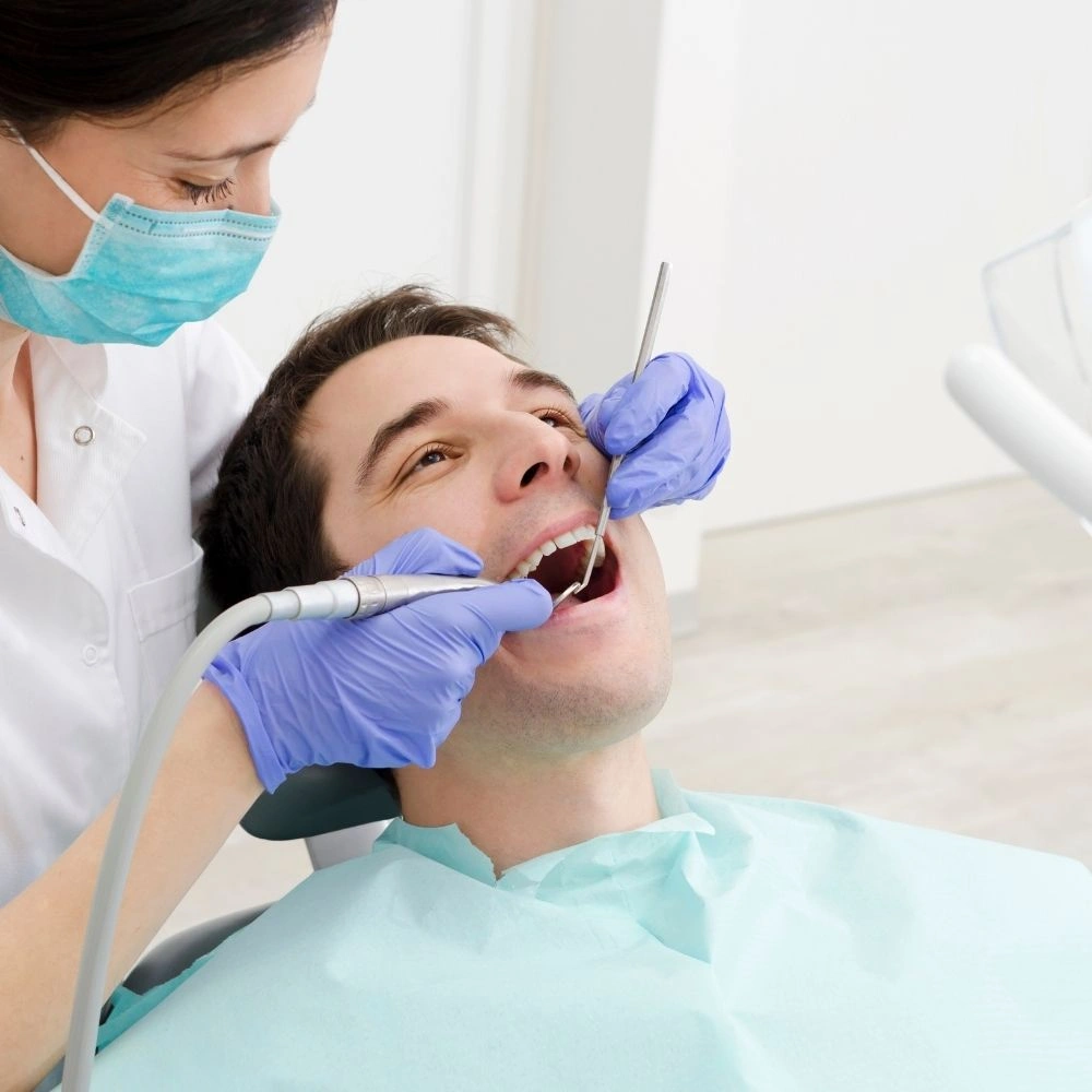 A dentist performing a professional dental cleaning on a male patient at Dental Art Clinic in Cambridge, showing the use of dental instruments during oral hygiene care.