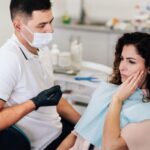 Dentist examining a patient holding her cheek in pain during an emergency toothache visit in Cambridge