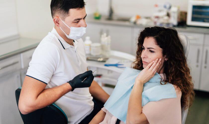Dentist examining a patient holding her cheek in pain during an emergency toothache visit in Cambridge