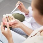Person holding a dental implant model while explaining tooth replacement treatment