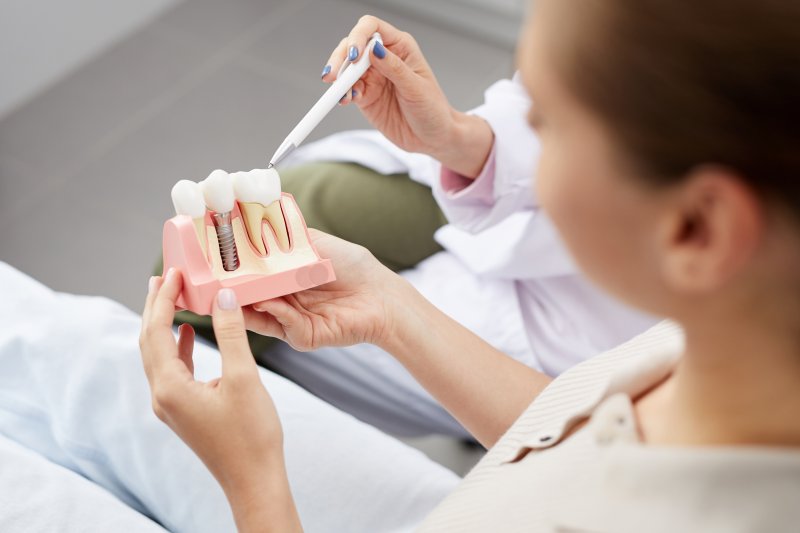 Person holding a dental implant model while explaining tooth replacement treatment